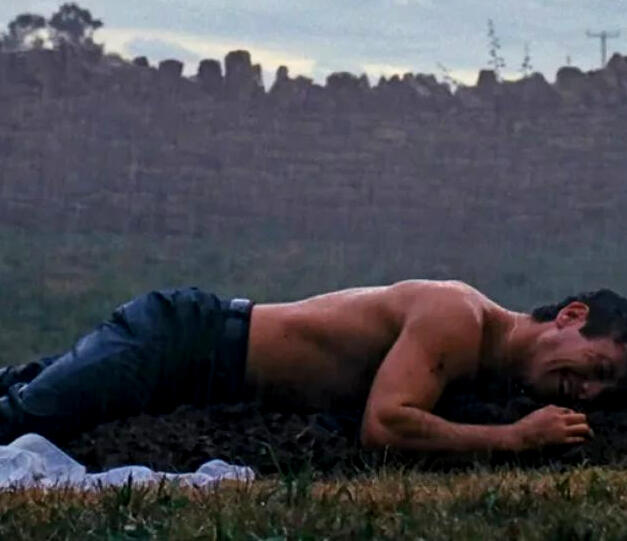 a still from the film "saltburn" depicting its protagonist, half-dressed, lying on top of a fresh grave, in tears